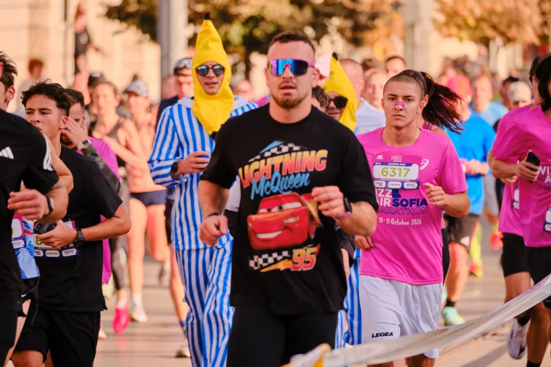 A runner in black and mirrored sunglasses beside a participant in a blue striped costume.