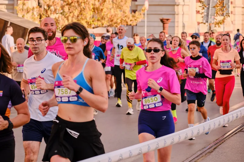 A woman in a blue running vest passing beside the race tape.