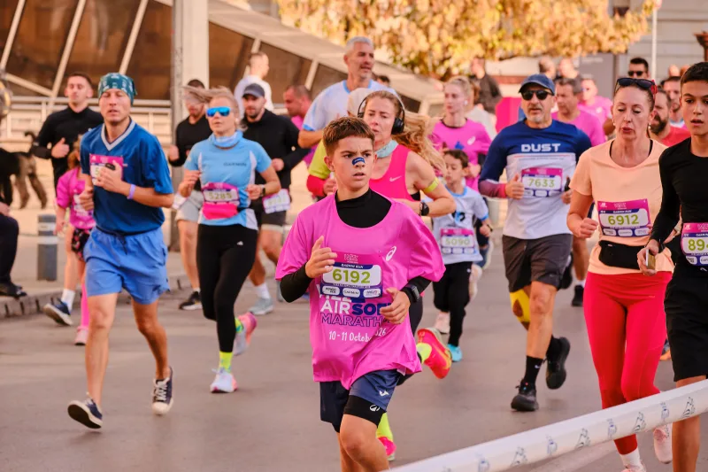 A young participant in pink approaching ahead of a busy running field.