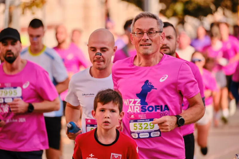 A young participant in red running beside an older runner in pink.