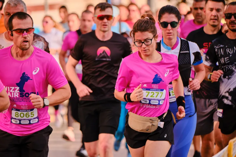 A runner in a pink cropped shirt looking down as she runs.