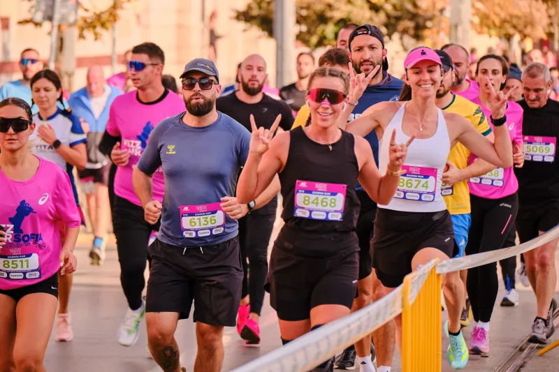 A runner in black raising his hands beside other participants.