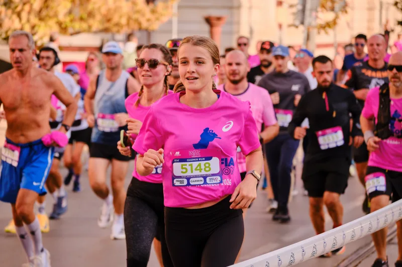 Two women in pink event shirts running together in sunlight.