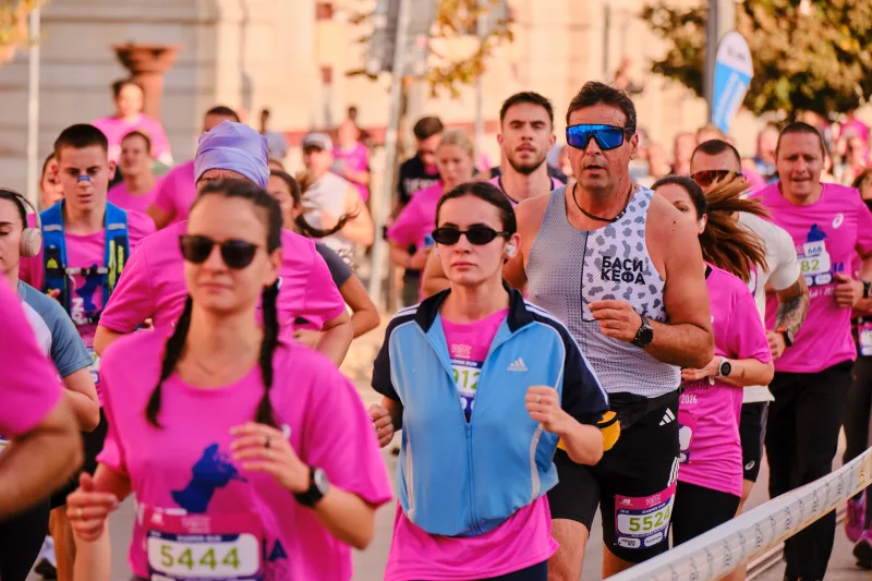 Two women wearing sunglasses running in pink shirts and a blue vest.