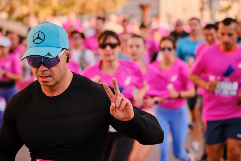 A runner in a turquoise cap and black top making a peace sign.