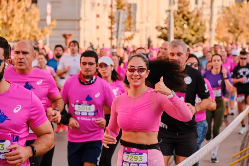 A smiling runner in a pink cropped top raising her hand.