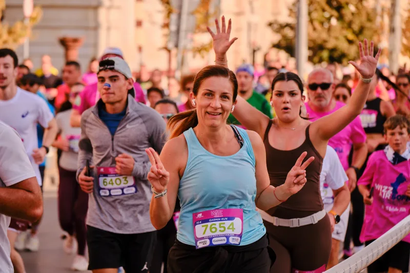 A smiling woman in turquoise running beside a participant waving at the camera.