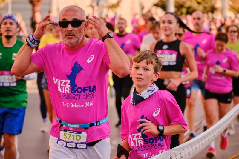 An older runner in sunglasses raising both hands beside a young participant.