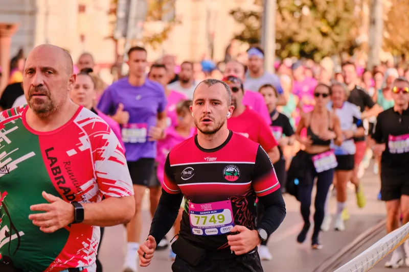 A runner in a red-and-black striped shirt among participants in pink.
