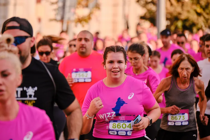 A smiling woman in a pink event shirt running through the crowd.