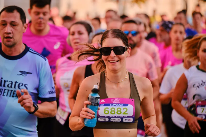 A smiling woman in black holding a blue bottle as she runs.