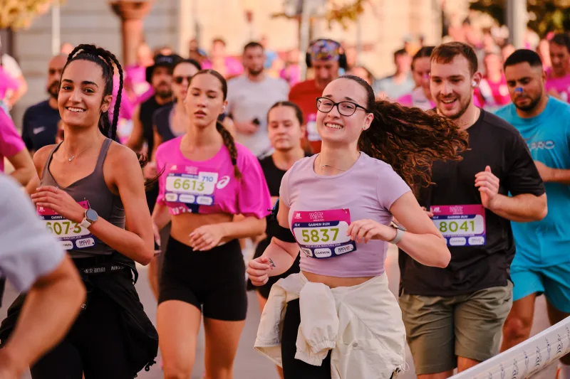 A woman in glasses and a pale shirt running with a jacket tied around her waist.