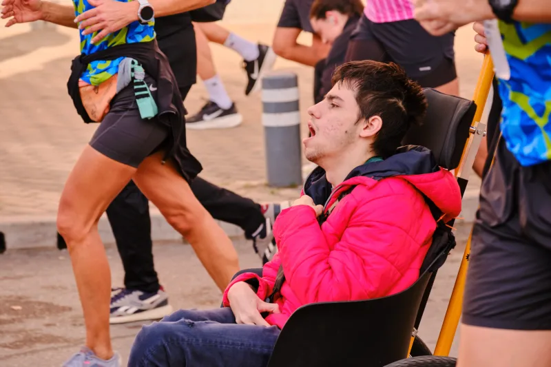 A participant in a wheelchair wearing a bright red jacket among the runners.