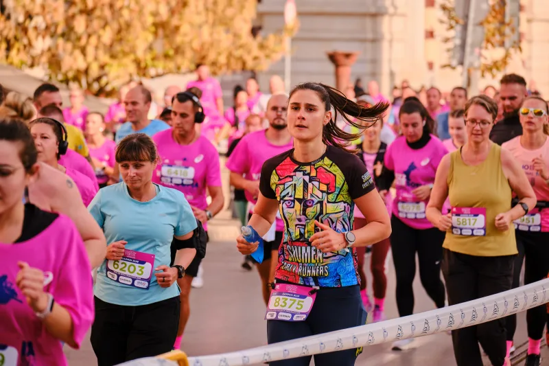 A participant in a colourful patterned shirt running beside the race tape.