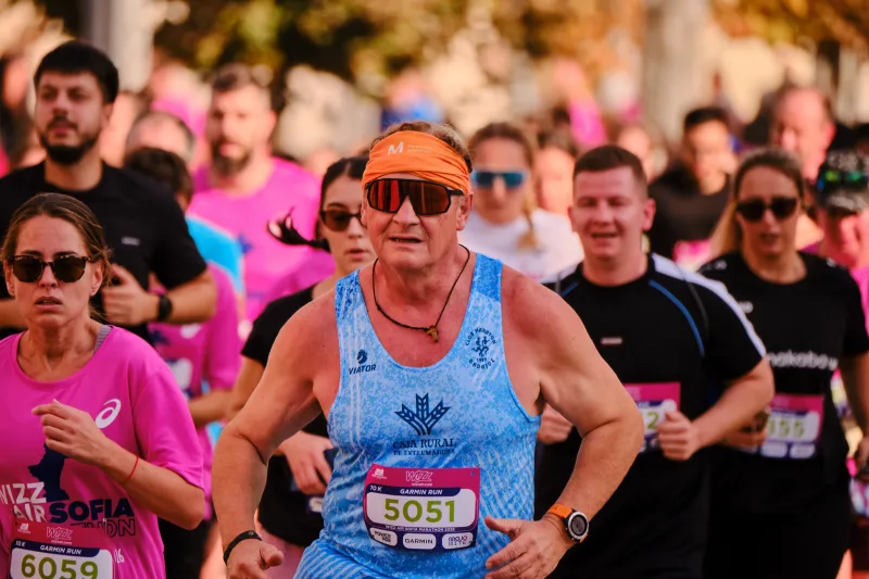 An older runner in a blue vest and sunglasses moving through the crowd.