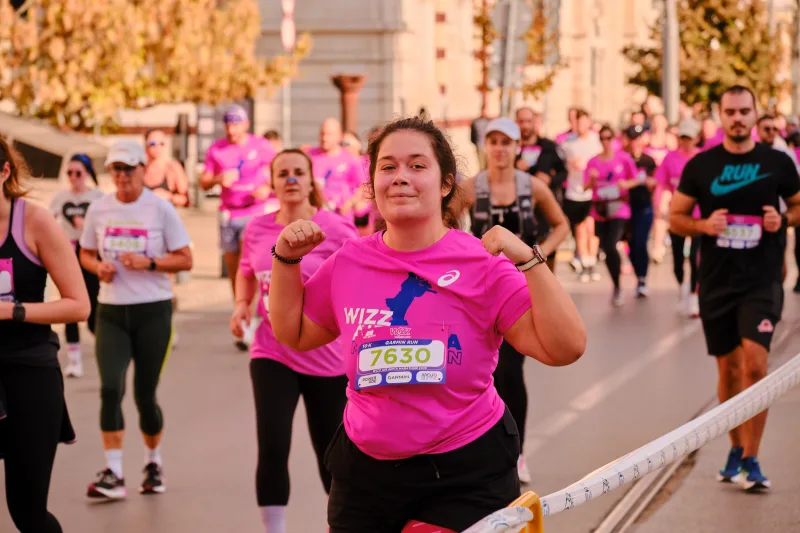 A smiling participant in pink raising both arms as she runs.