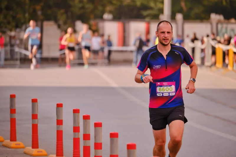 A runner in a dark multicoloured shirt beside red-and-white bollards.