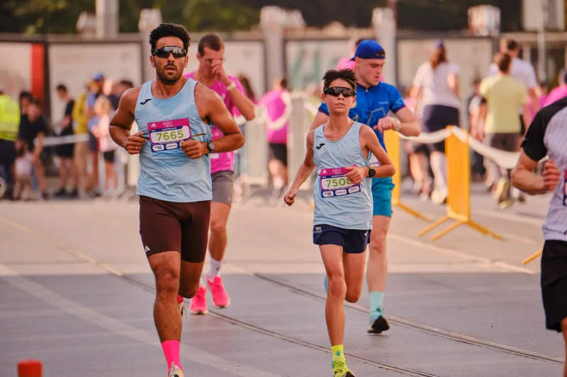 A man and a young participant running in matching pale blue vests.