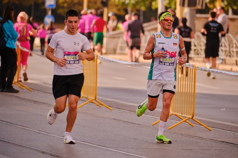 Two runners in pale shirts approaching side by side on the street.