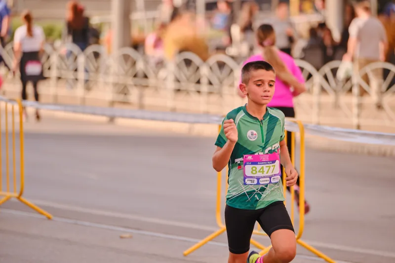 A young participant in a green sports shirt running beside the barriers.