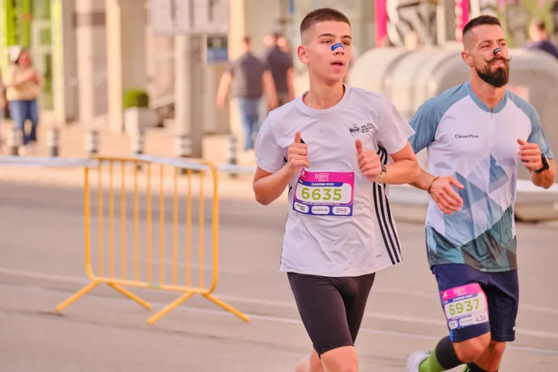 Two runners in pale grey tops approaching near the race barriers.
