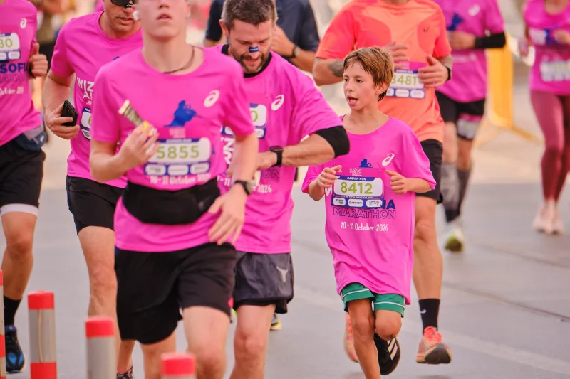 A young participant in pink and green shorts running among adults in matching pink.