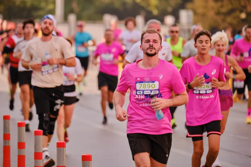 A smiling runner in a pink shirt approaching beside red-and-white bollards.