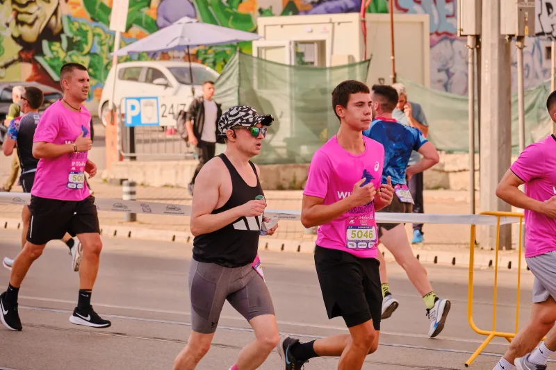 A side view of a woman in black running beside a young participant in pink.