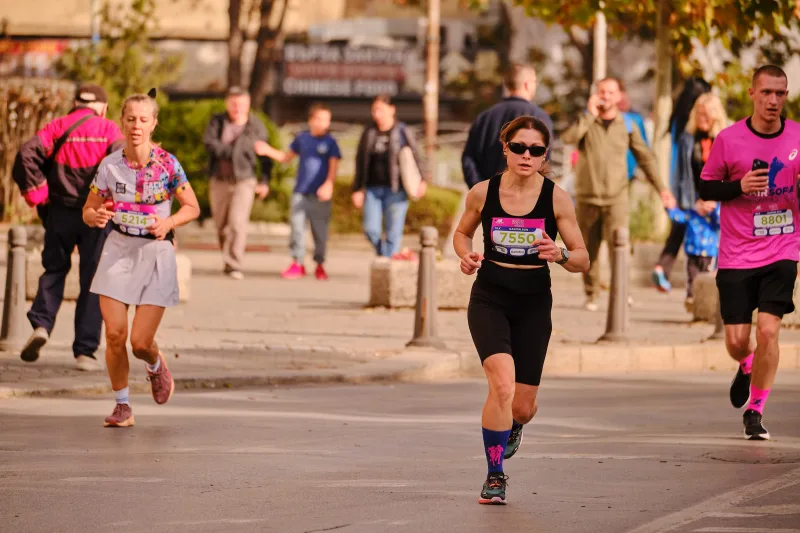 A woman in black and sunglasses running beside the tram tracks.