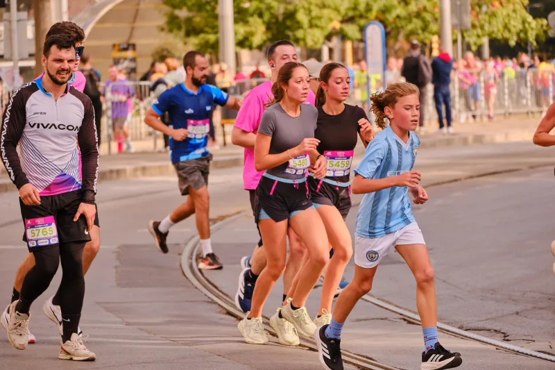 A young participant in a pale blue football shirt running beside a woman in dark sportswear.