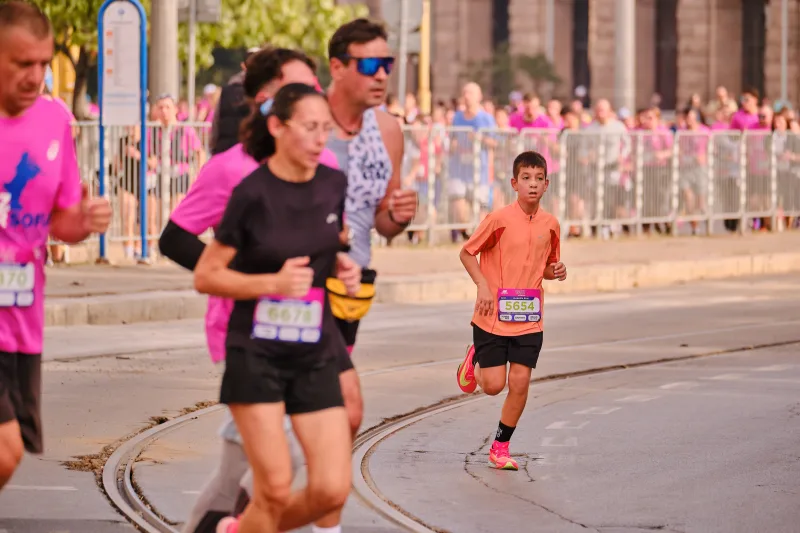 A woman in black running ahead of a young participant in an orange shirt.